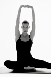Model Alena Blohm stretching overhead in a black tank top and leggings on an exercise mat against a bright white background.