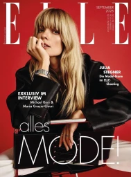 Julia Stegner wearing a black leather jacket seated on a chair against a bold red background for Elle Germany.