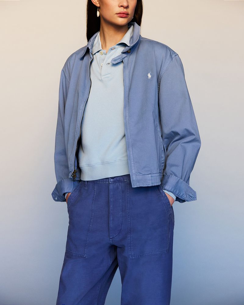 Adult female wearing a blue jacket, light blue polo shirt, and blue pants in a studio setting, looking directly at the camera.