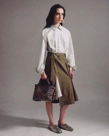 Fashion photo of a stylish woman in a striped shirt and khaki skirt, accessorized with a leopard bag and snake print shoes against a grey backdrop.