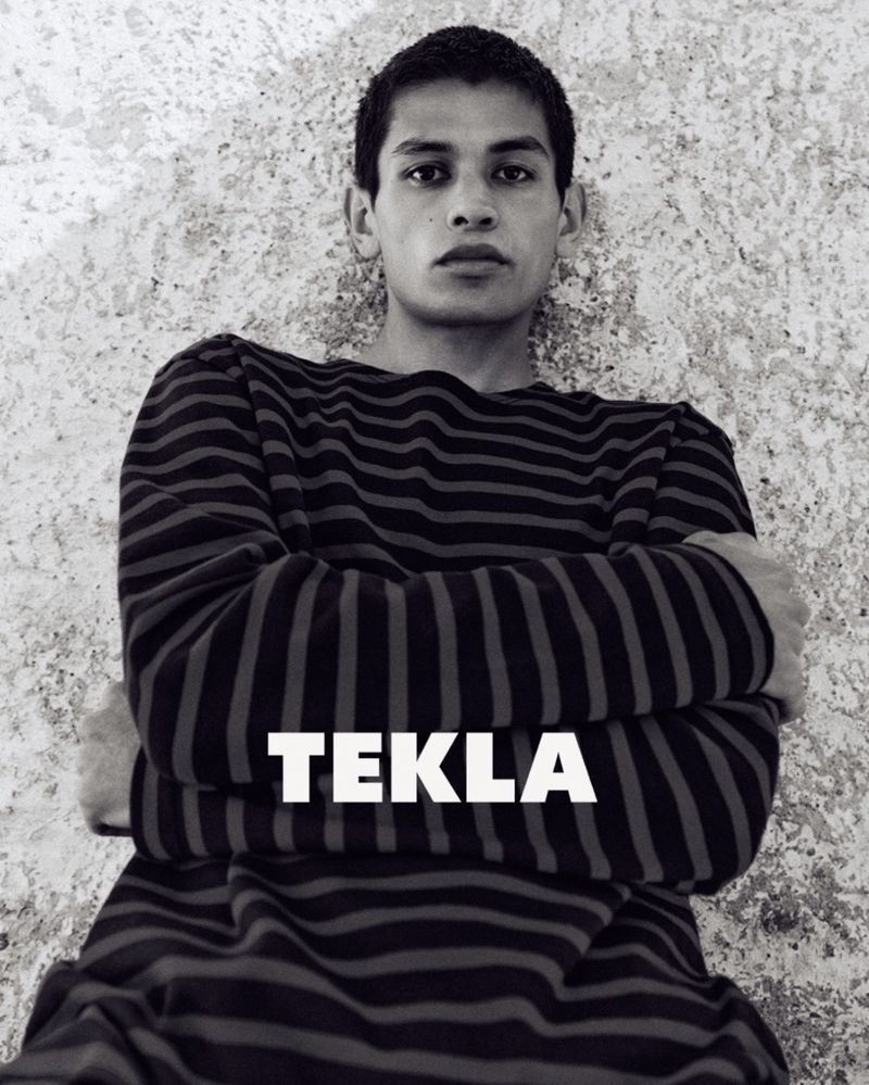 Model Sakua Kambong wearing a dark striped long-sleeve top against a textured stone wall for Tekla.