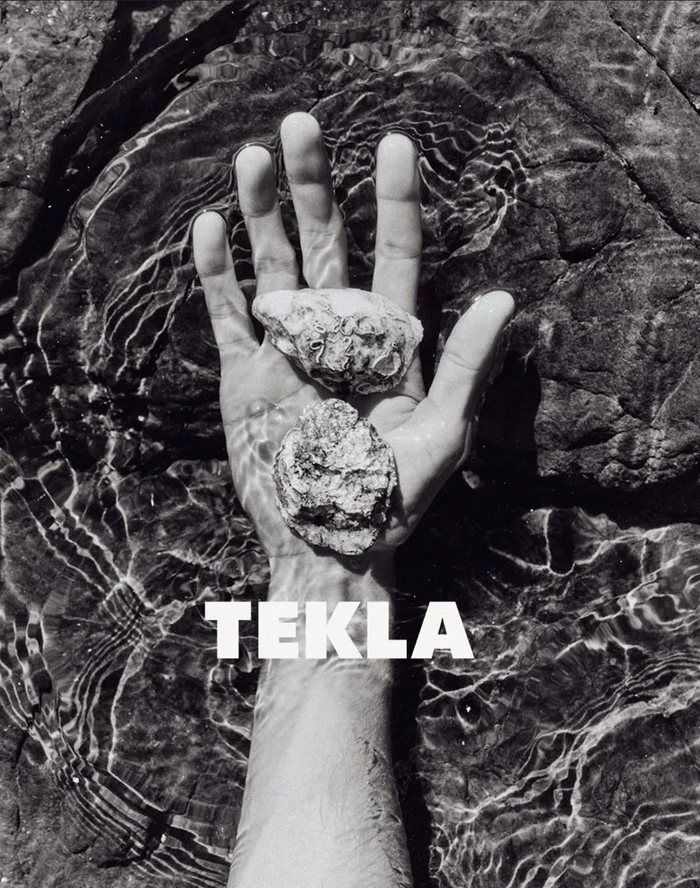 Black and white photo of an open hand holding two rough textured stones in shallow water with Tekla text overlay.