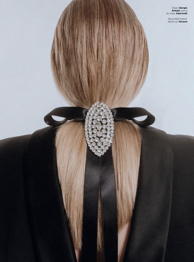 Rear view of a model with straight blonde hair tied with a black satin bow and an oval crystal hairclip against a light background.