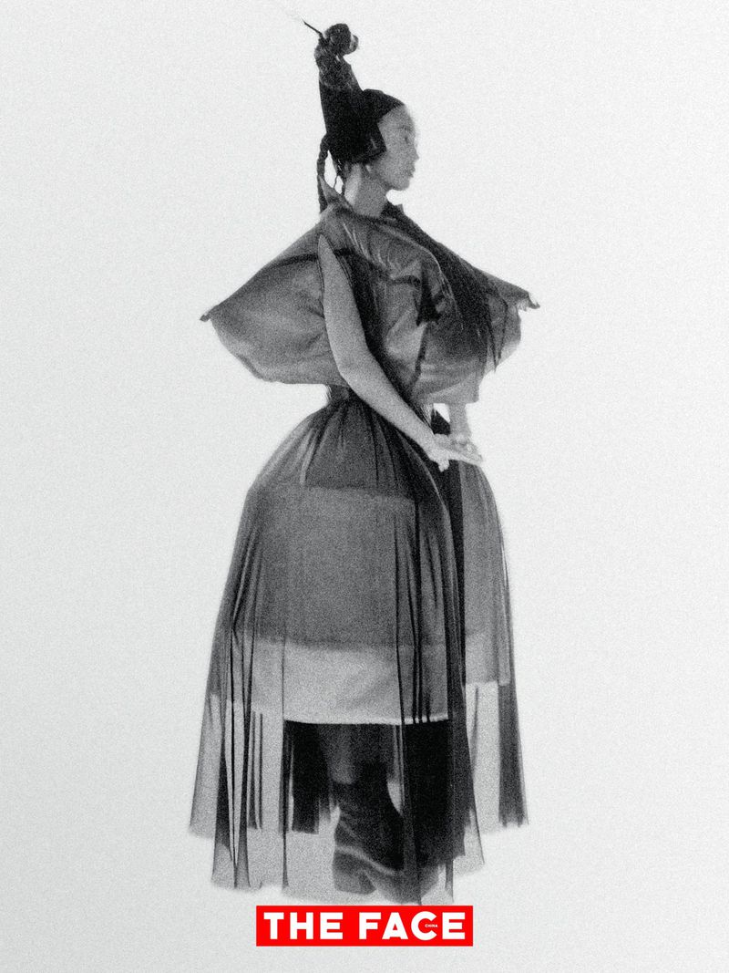 Model wearing a sculptural black avant-garde voluminous gown and tall headpiece against a stark white backdrop.