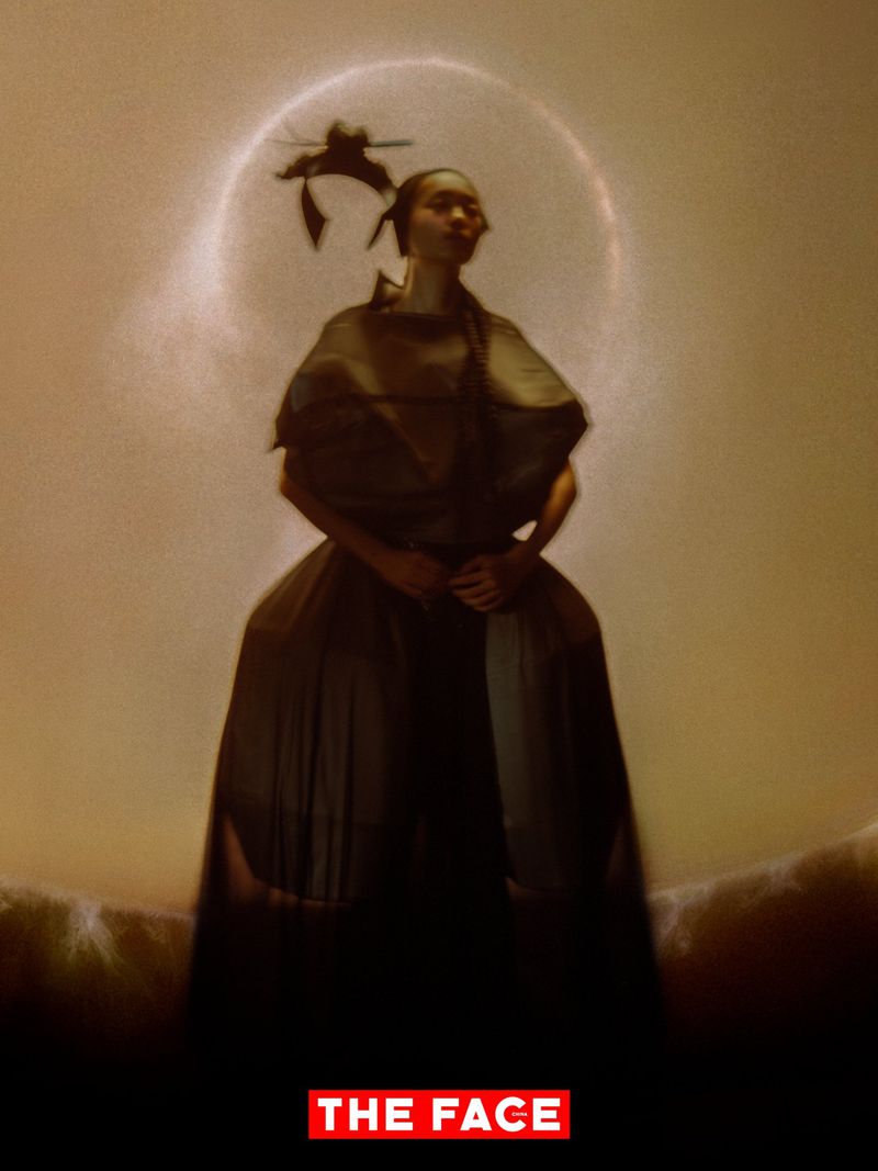 Model in a voluminous sculptural dark gown standing against a warm glowing halo backdrop for The Face China.