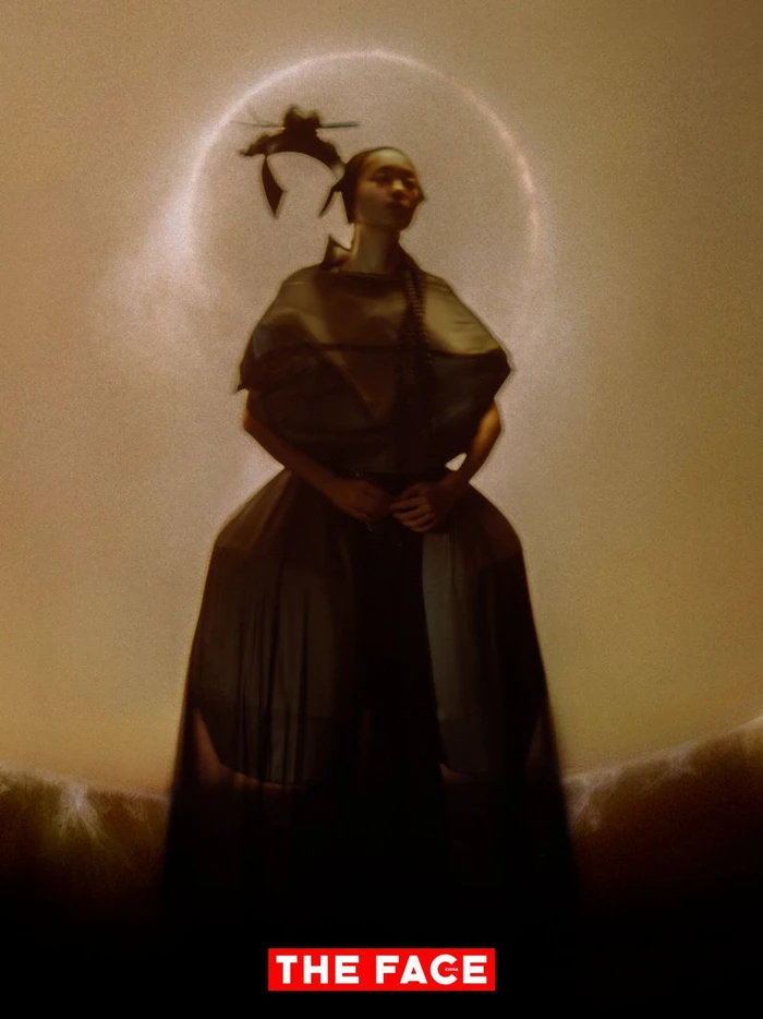 Model in a voluminous sculptural dark gown standing against a warm glowing halo backdrop for The Face China.
