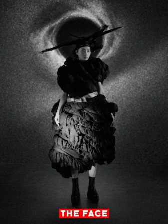 Model wearing a voluminous sculpted black dress and horizontal headpiece standing before a celestial vortex backdrop.