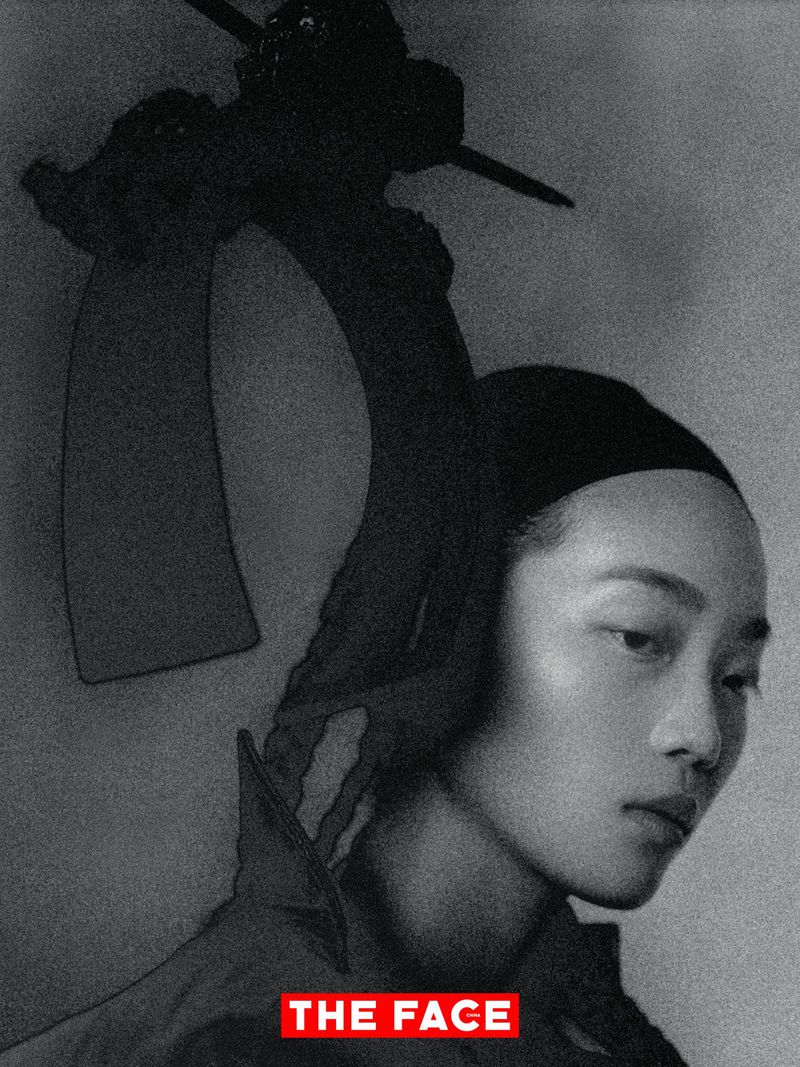 East Asian model wearing a dramatic black sculptural headpiece in a monochrome editorial portrait.