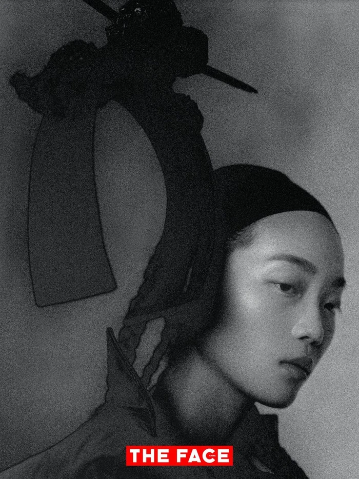 East Asian model wearing a dramatic black sculptural headpiece in a monochrome editorial portrait.