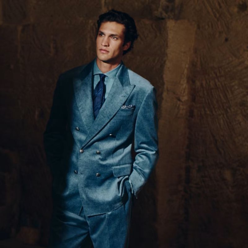 Francisco Henriques wearing a light blue double-breasted velvet suit and dark tie against a rustic stone wall.
