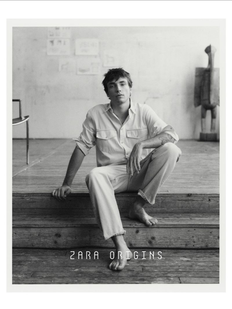 Young man in a button-down shirt and trousers sitting on wooden steps in a studio, Zara Origins campaign photograph.