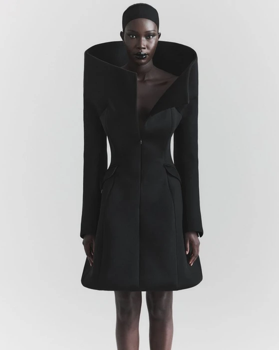 Model Adhel Bol in a sculptural black flared coat with an exaggerated high collar against a neutral studio backdrop.