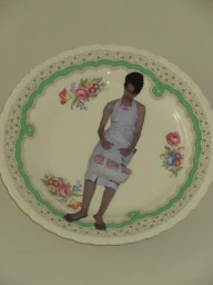 A vintage floral ceramic plate printed with an image of a model wearing a white apron dress against a cream background.