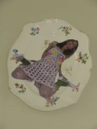 Vintage floral ceramic side plate with a collaged cutout of a woman in a floral top and pink skirt against a plain background.