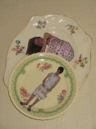 Two vintage floral ceramic plates displaying printed fashion editorial photographs of models against a plain cream background.