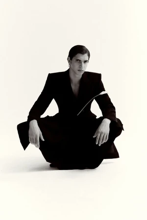 Model Hedi Ben Tekaya crouching in a tailored black suit against an unbroken white studio backdrop.