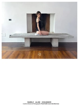 Young woman in black leotard poses on concrete bench in bright room with parquet floor and white walls, minimalist design.