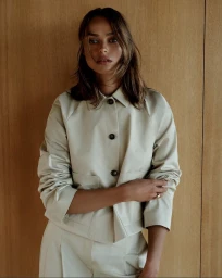 Model Birgit Kos wearing a cream button-up jacket against a warm wood paneling wall for Goop campaign.