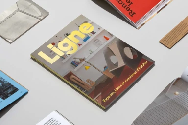 Ligne magazine cover with yellow typography surrounded by printed editorial booklets on a flat neutral surface.