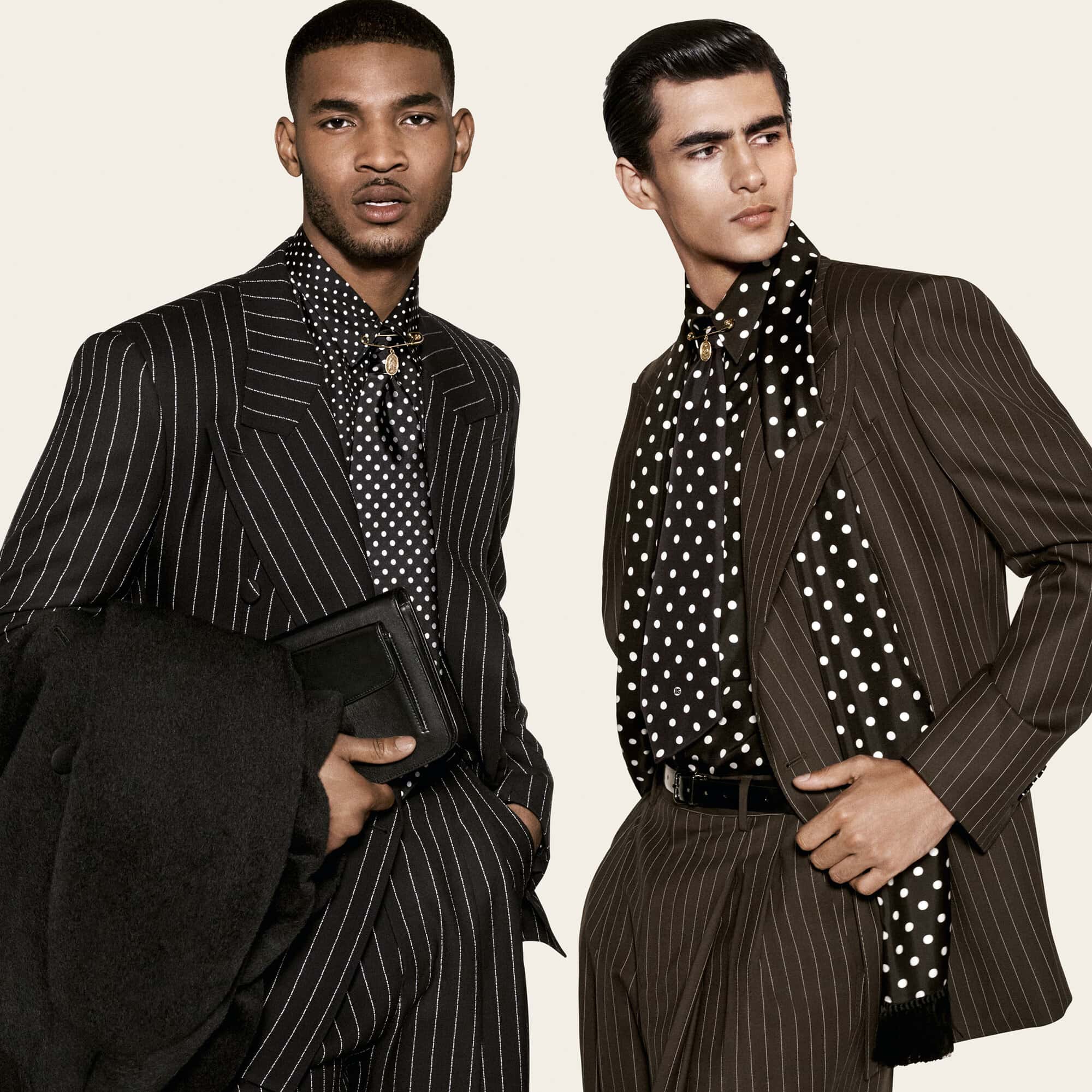 Two male models posing in tailored pinstripe suits and black-and-white polka dot shirts against an off-white background.