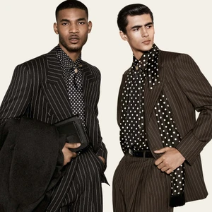 Two male models posing in tailored pinstripe suits and black-and-white polka dot shirts against an off-white background.