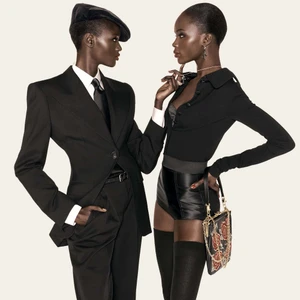 Two Black models in black tailored Dolce & Gabbana outfits posing against a neutral seamless studio backdrop.