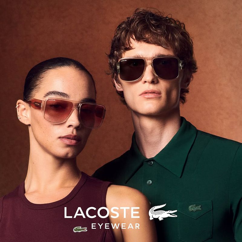Two fashion models pose wearing Lacoste eyewear against a warm brown backdrop showcasing the brand's sunglasses collection.