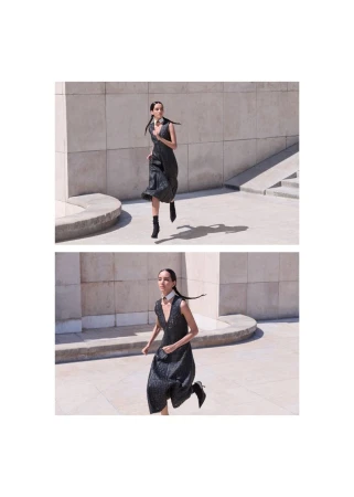 Model Eduarda Vieira running in a sleeveless black midi dress and ankle boots across a sunlit stone courtyard.