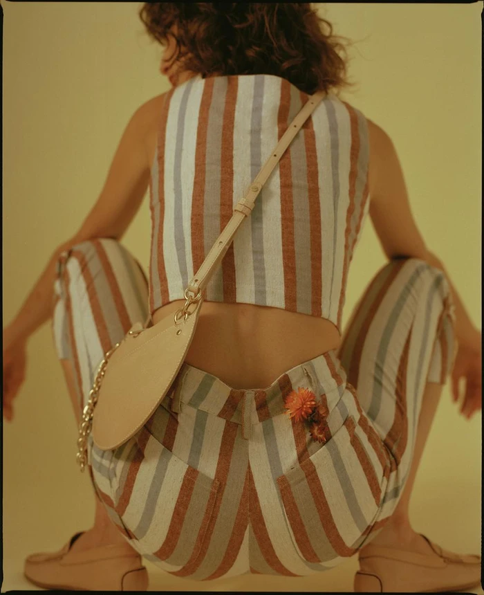 Model from behind wearing a striped top and trousers with a leather crossbody bag against a plain yellow background