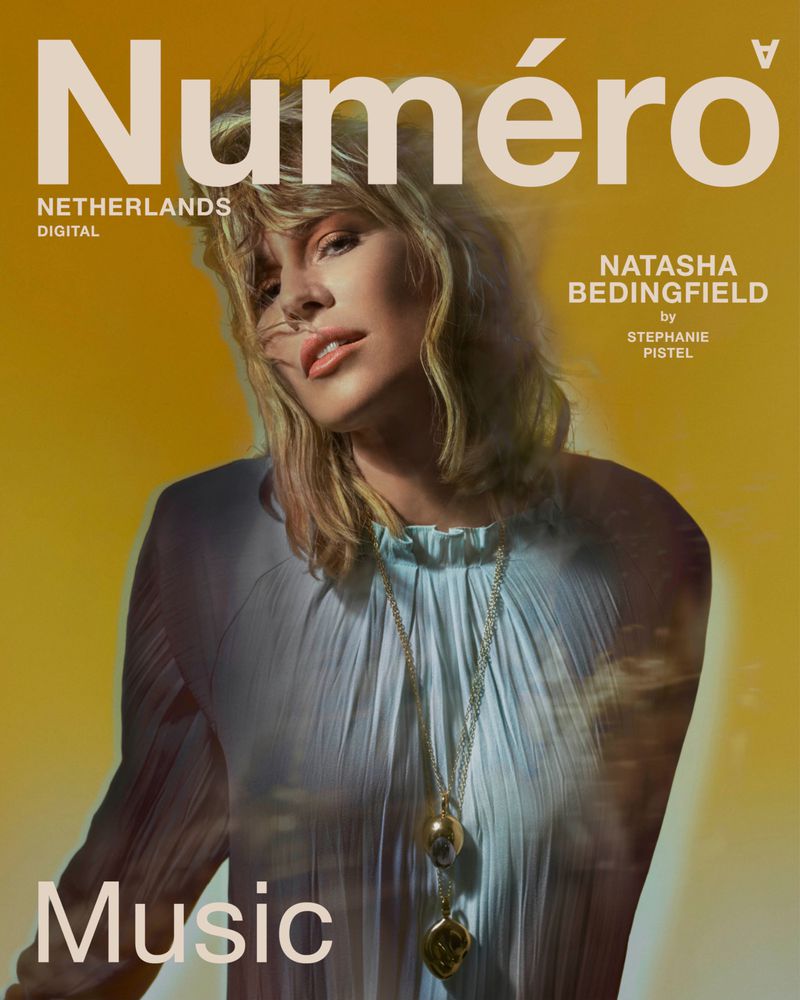 Natasha Bedingfield posing for Numéro Netherlands Digital in a pleated light blue blouse against a vibrant yellow backdrop.