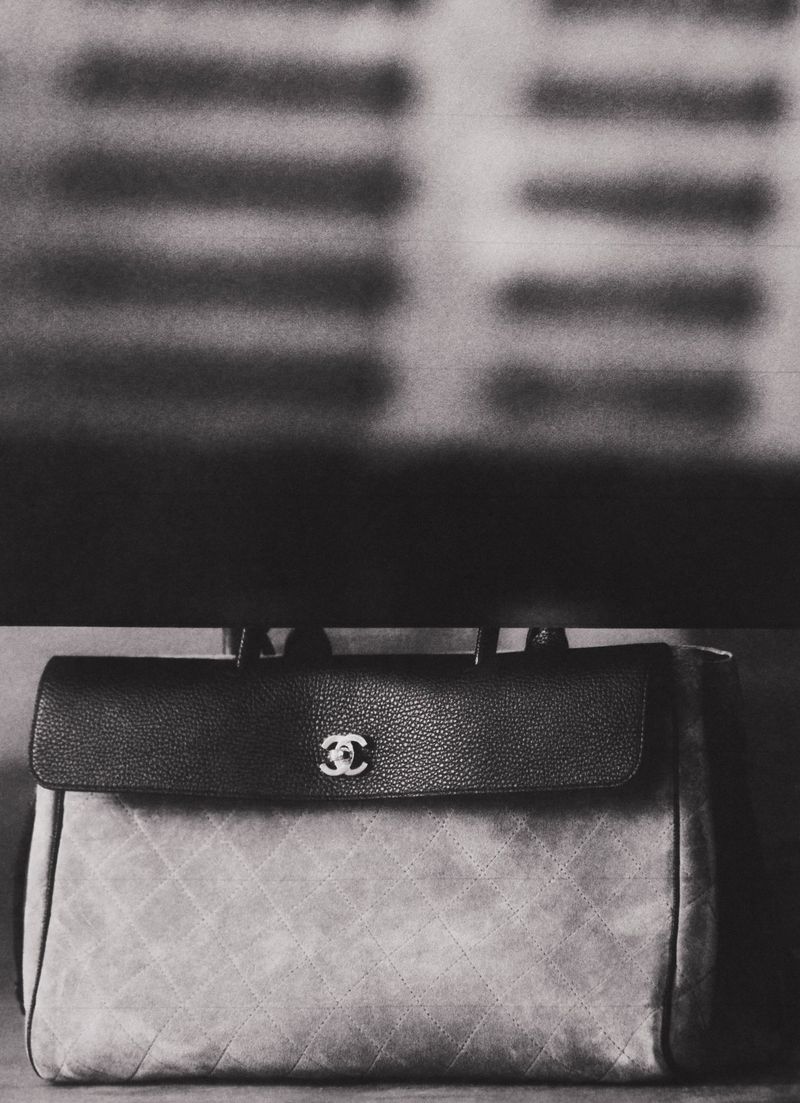 Black and white photograph of a quilted Chanel handbag with a pebbled leather flap and metallic logo closure resting on a surface.