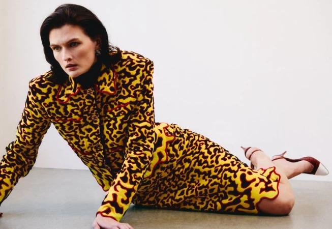 Model Lara Mullen posing on the floor wearing a yellow and black patterned skirt suit in a bright studio.