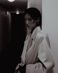 Woman in trench coat leaning against a wall in a dimly lit hallway for Numero Netherlands