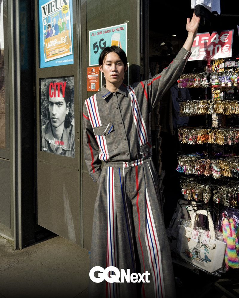 Model Ikko Ohira in a grey striped matching shirt and wide-leg trousers posing outside a Parisian souvenir shop.
