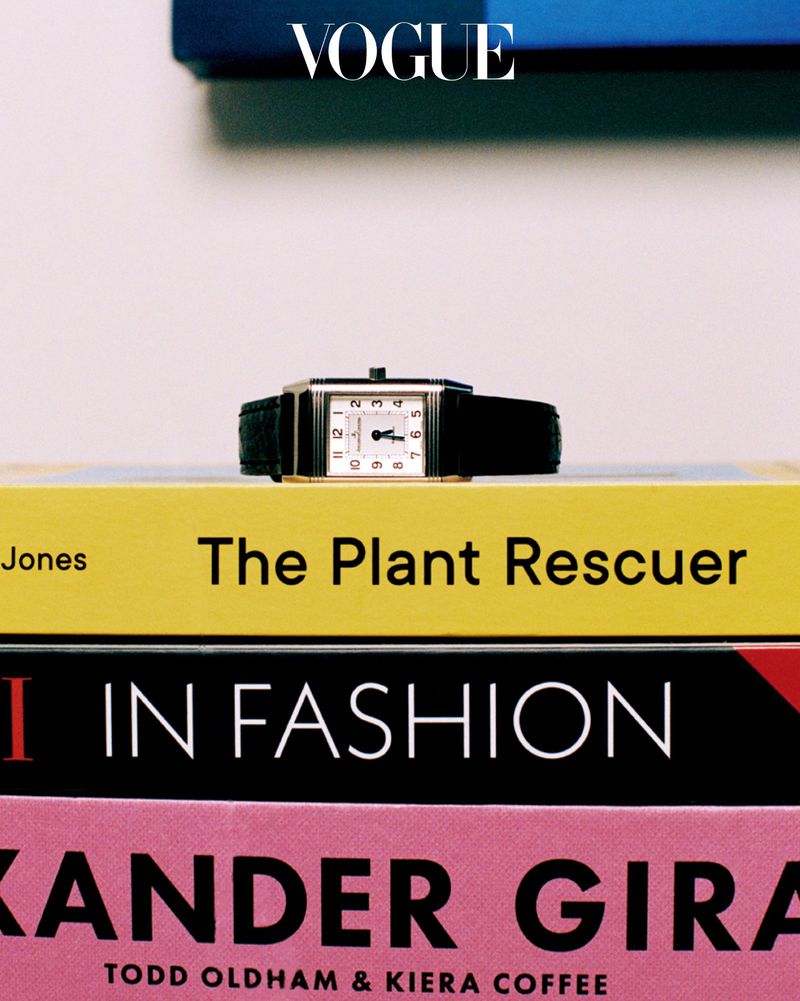 A rectangular luxury wristwatch with a black leather strap resting on top of a stack of colourful hardback books.