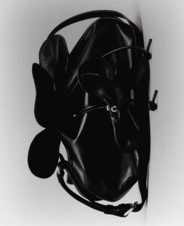 Black sculptural leather handbag with petal-shaped bow detailing against a neutral studio backdrop.