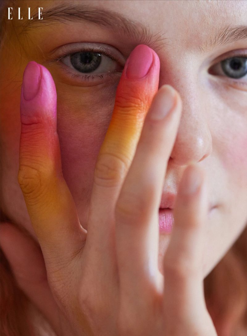 Close-up shot of a Caucasian female model with painted fingertips covering half her face in a beauty/fashion editorial with ELLE logo.