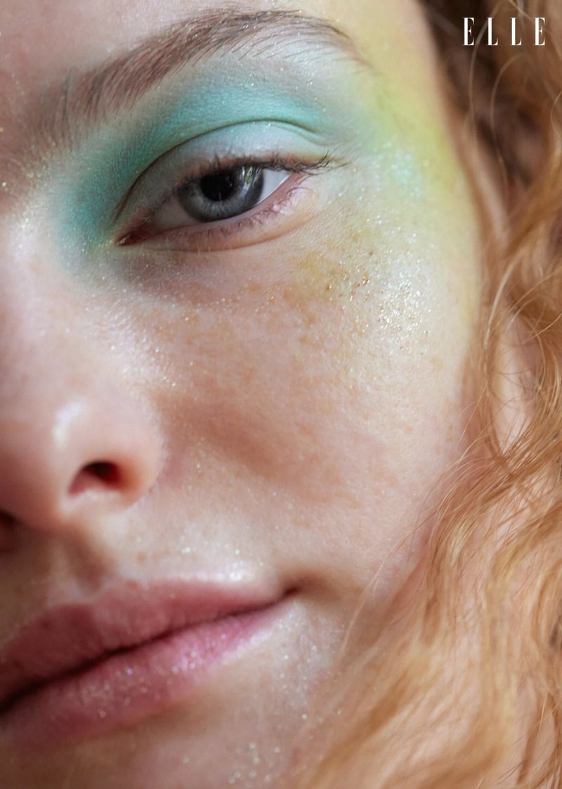 Close-up of a woman's face with eye shadow and glossy lips, creating a beauty shot with natural skin texture and the 'ELLE' logo.