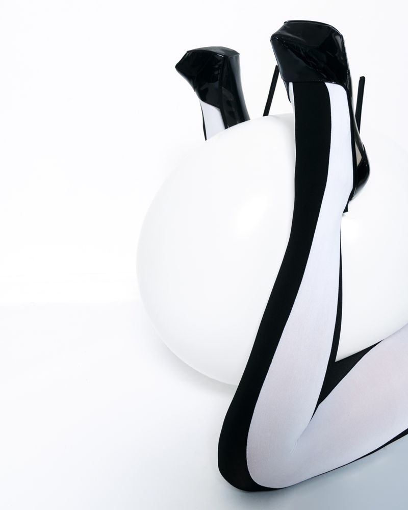 Fashion shot featuring a woman's legs in black-and-white tights and high heels, resting on a white exercise ball in a studio setting.