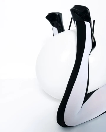 Fashion shot featuring a woman's legs in black-and-white tights and high heels, resting on a white exercise ball in a studio setting.