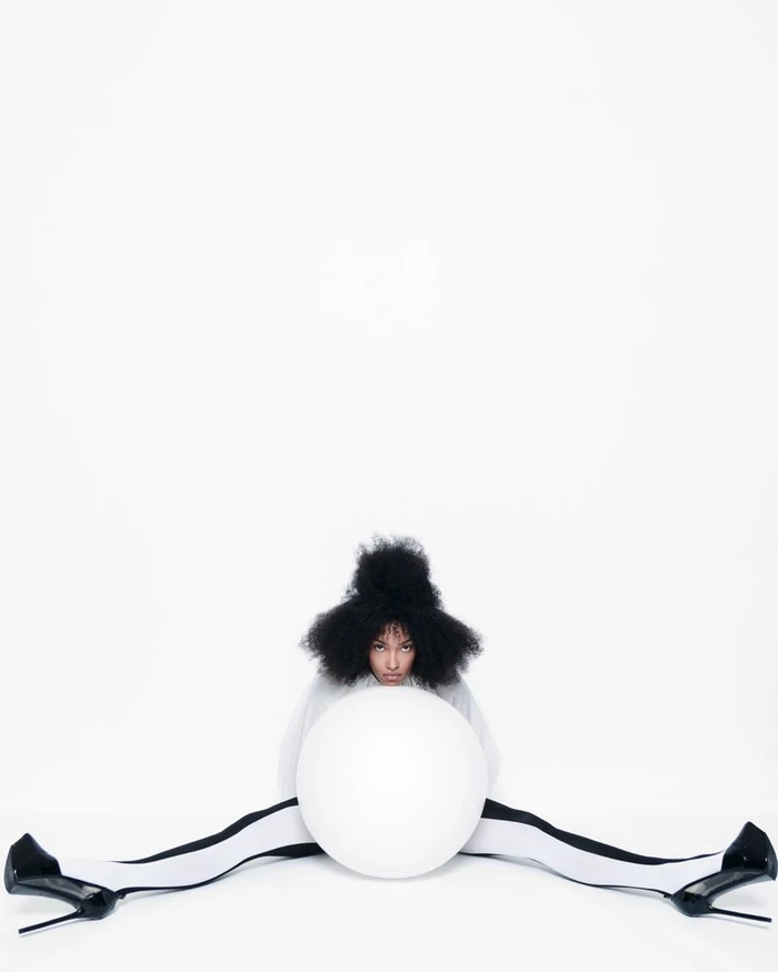 Model with voluminous dark hair holding a large white sphere against a plain white background