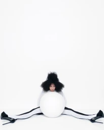 Model with voluminous dark hair holding a large white sphere against a plain white background