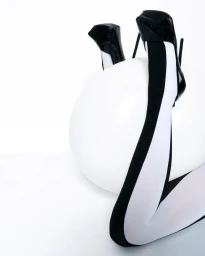 Model's legs upside down in black-and-white tights and black heels posed around a large white sphere against a white background.