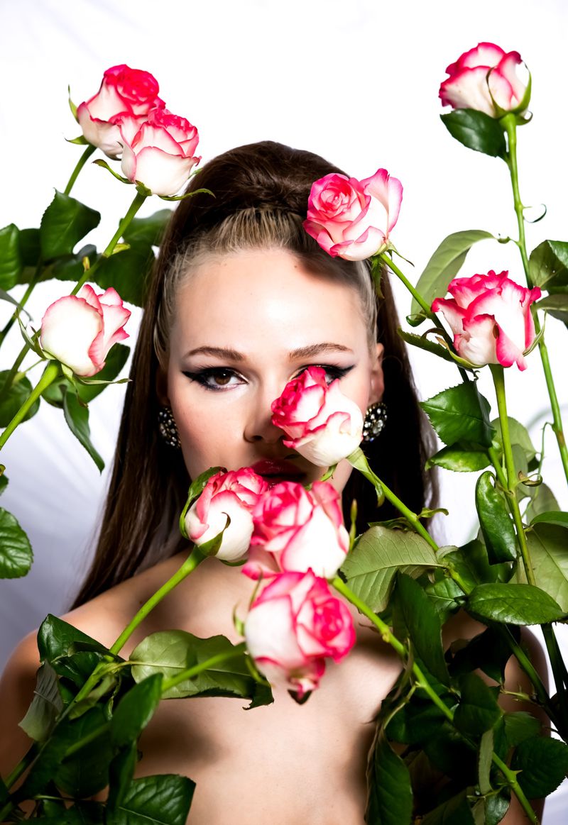 Brunette woman poses with pink and white roses in a close-up studio portrait against a white backdrop, beauty shot, fashion concept.