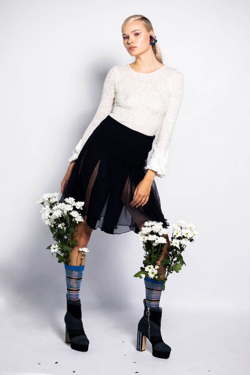 Fashionable woman in stylish clothes and platform boots with flower-filled socks in a studio setting against a white background.