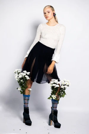 Fashionable woman in stylish clothes and platform boots with flower-filled socks in a studio setting against a white background.