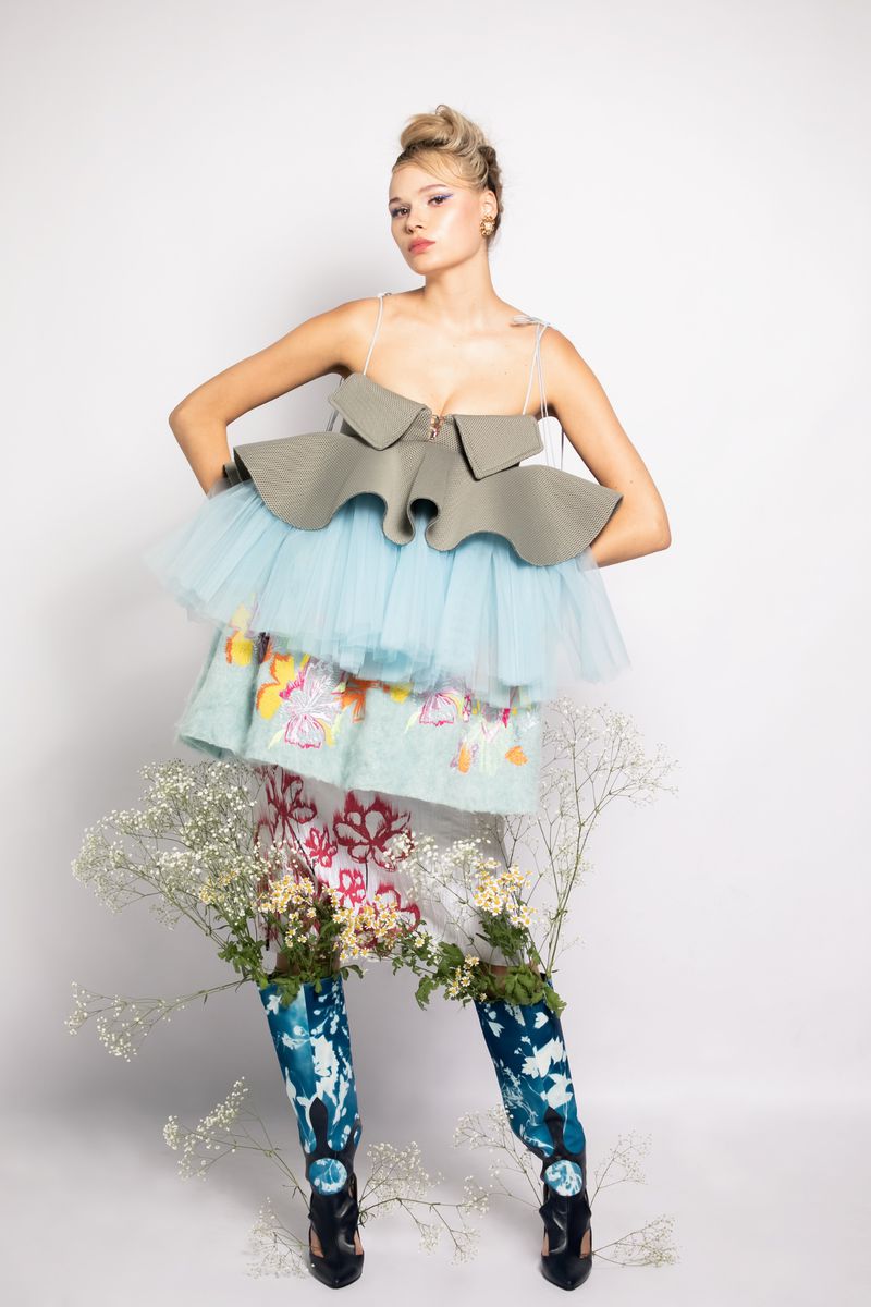 Young adult woman in ruffled top and floral skirt poses in front of a white backdrop in studio lighting, fashion concept.