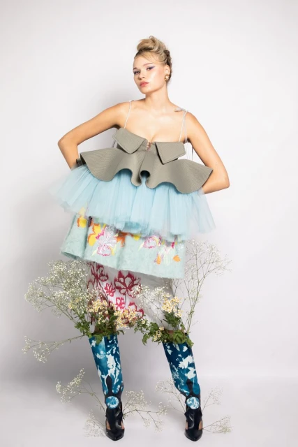 Young adult woman in ruffled top and floral skirt poses in front of a white backdrop in studio lighting, fashion concept.