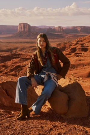 Mathilde Henning seated on a rock wearing a brown jacket and blue denim jeans in a desert landscape with red buttes.
