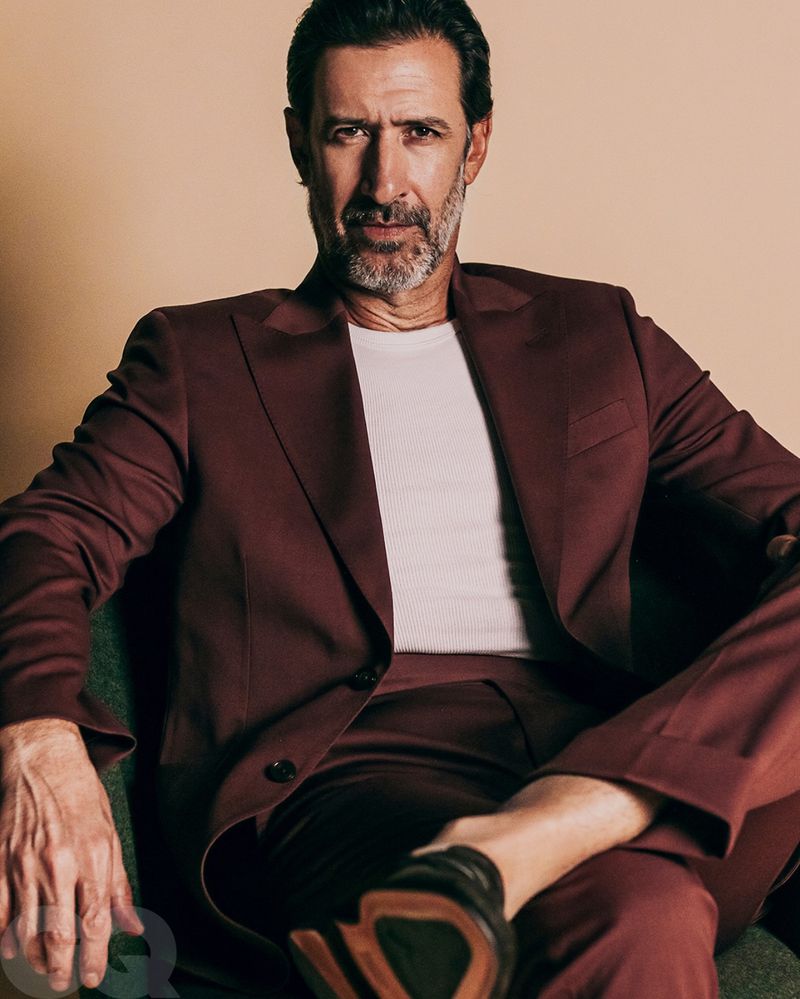 Portrait of a mature man in a burgundy suit, seated indoors, looking at the camera with a neutral expression.